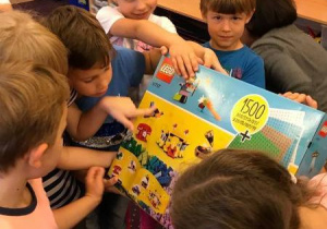 Zdjęcie zrobione w sali przedszkolnej. Dzieci wspólnie trzymają pudełko klocków LEGO, które dostały od rodziców. Zdjęcie nie jest pozowane. Dzieci są uśmiechnięte i podekscytowane.